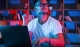 positive emotions. man in glasses and white shirt is sitting by the laptop in dark room with neon lighting